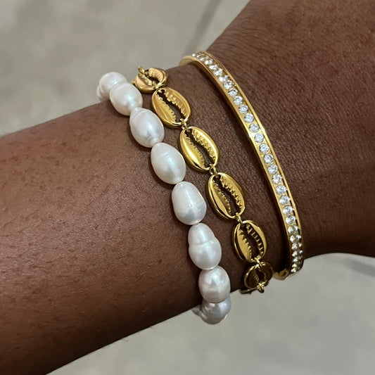Close-up of a wrist wearing two gold and pearl bracelets on a neutral background