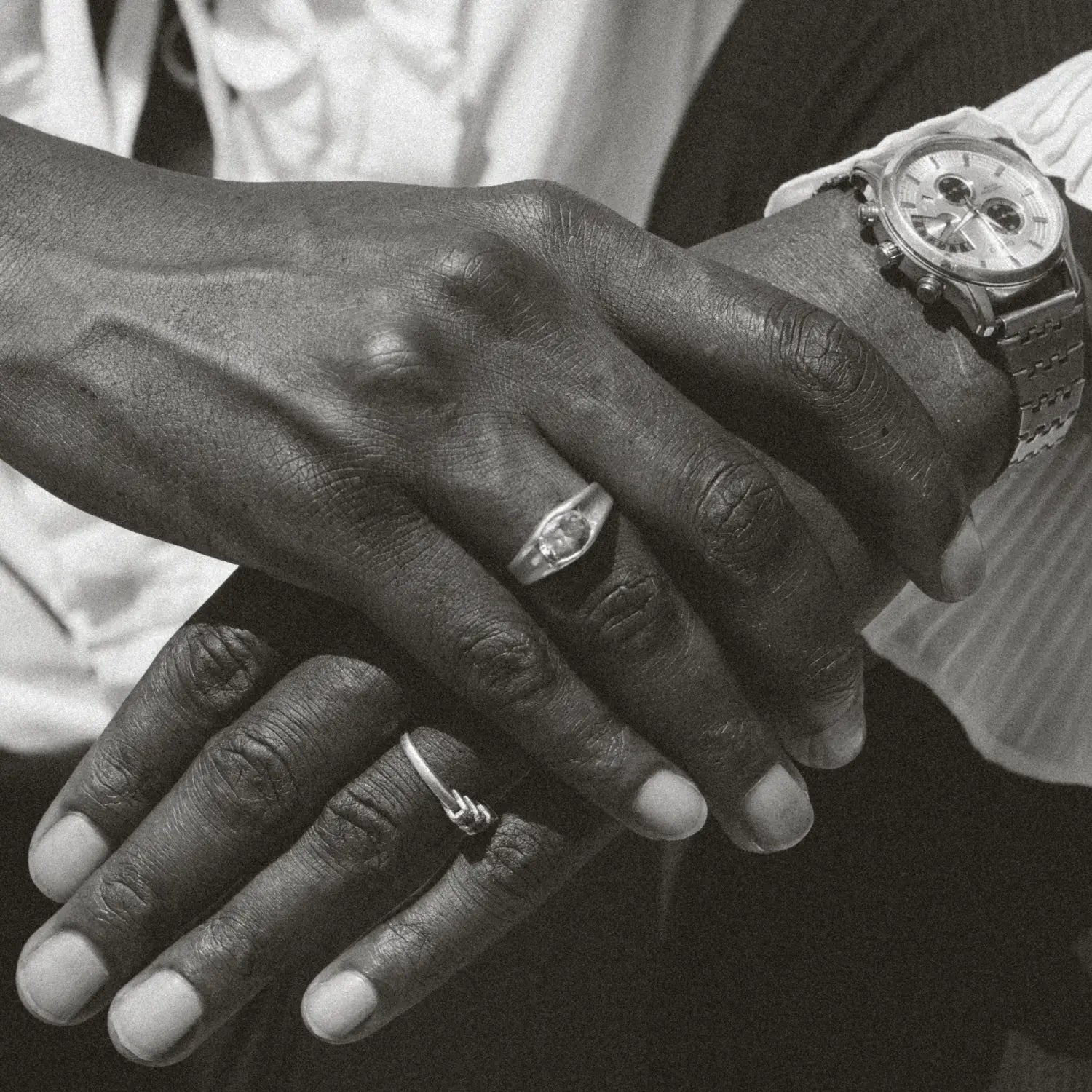 Close-up of two hands with wedding rings, one wearing a watch.