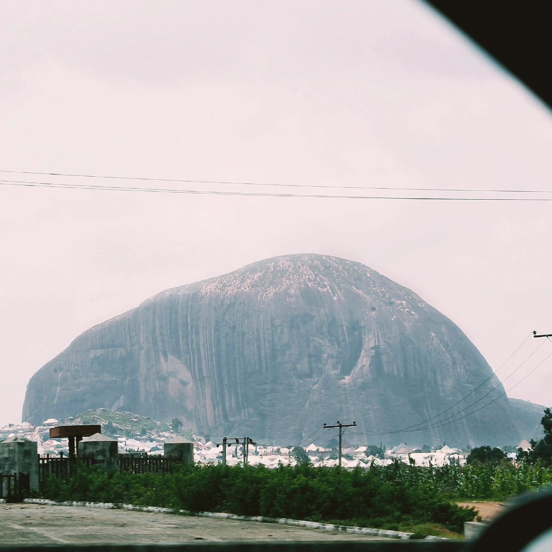 Large rocky outcrop with a cityscape at its base under a cloudy sky.